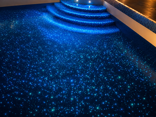 Swimming pool illuminated at night with glow-in-the-dark aggregate, creating a starry blue underwater effect across the pool floor and steps.